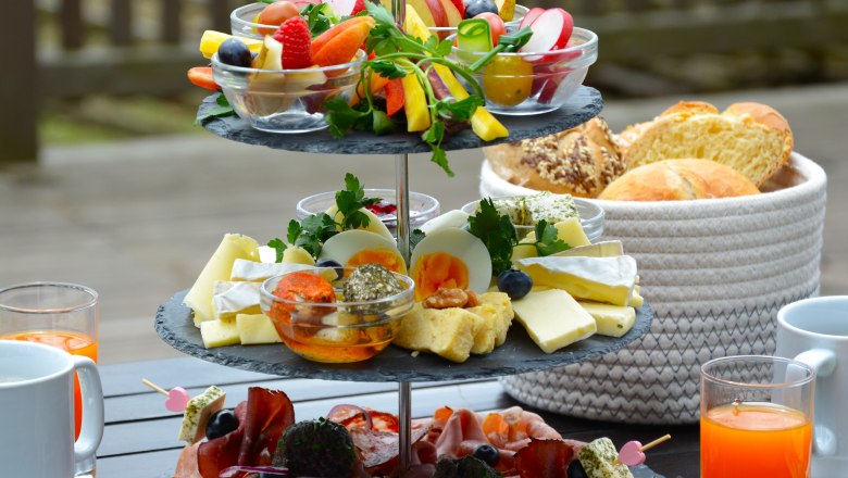 Etagere mit Aufschnitten, K&auml;se und Gem&uuml;se, daneben Getr&auml;nke und ein Brotkorb.