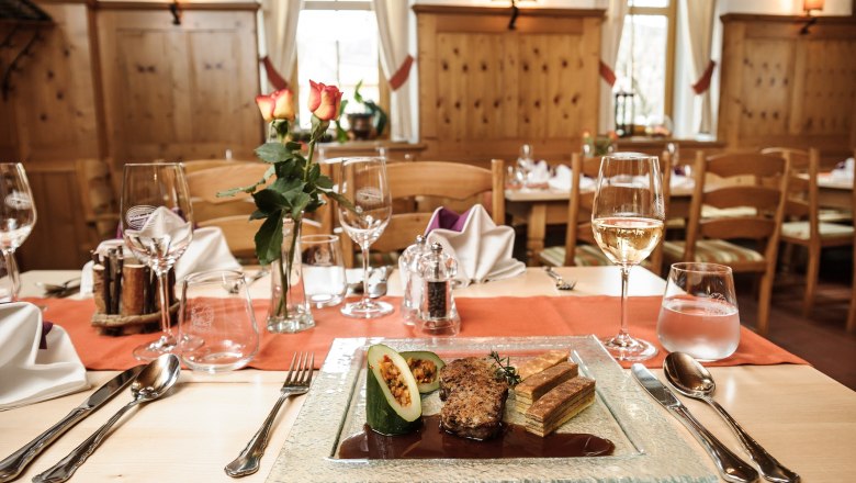 Ein elegant gedeckter Tisch in einem rustikalen Restaurant mit einem Teller Gourmet-Essen, Weingläsern und einer Vase mit Rosen.