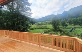 Blick von einer Terrasse auf eine grüne Landschaft mit Bäumen und Hügeln.