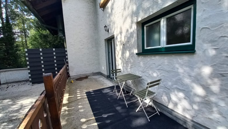 Terrasse einer Ferienwohnung mit Tisch und Stühlen, umgeben von Bäumen.