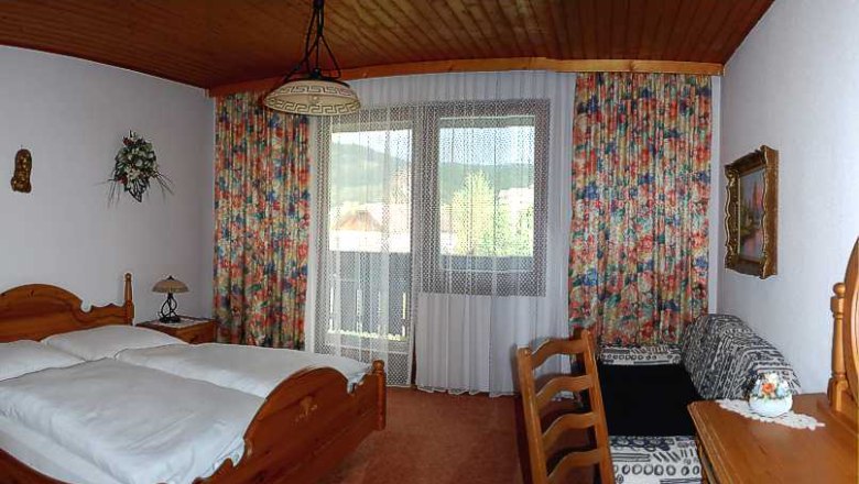 Gemütliches Hotelzimmer mit Holzmöbeln, Doppelbett, Balkon und bunten Vorhängen.
