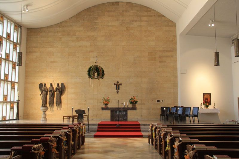 Innenansicht einer Kirche mit Altar, Bänken und religiösen Skulpturen.