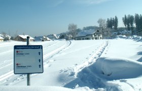 Winterlandschaft mit Langlaufloipe und Wegweiser in Bärnkopf.