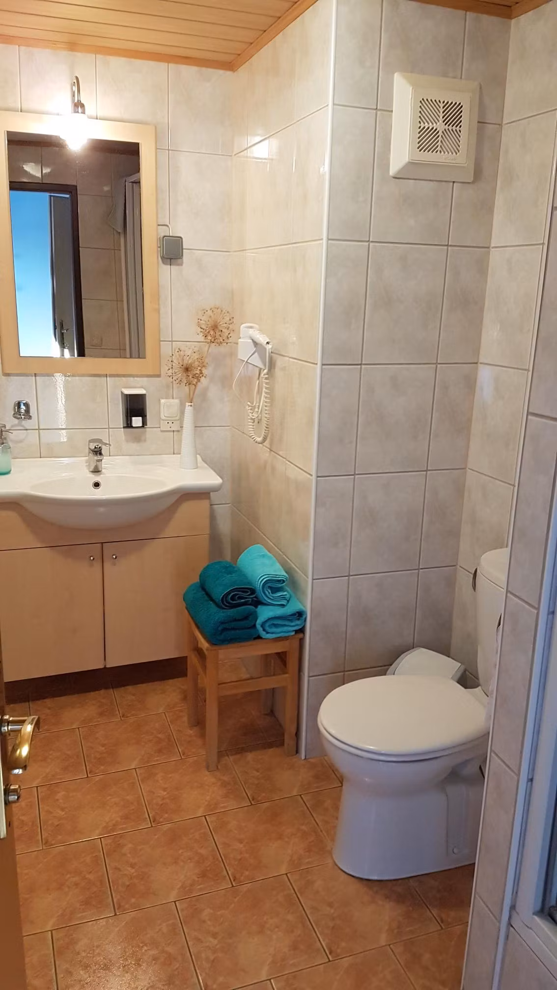 Ein Badezimmer mit Waschbecken, Spiegel, Toilette und Handtüchern auf einem Hocker.