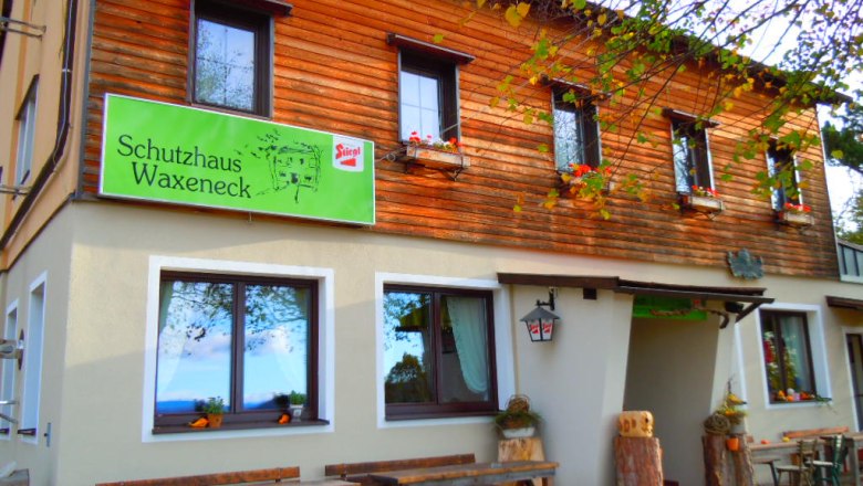 Eingang zum Schutzhaus Waxeneck mit Holztischen und Blumenk&auml;sten.