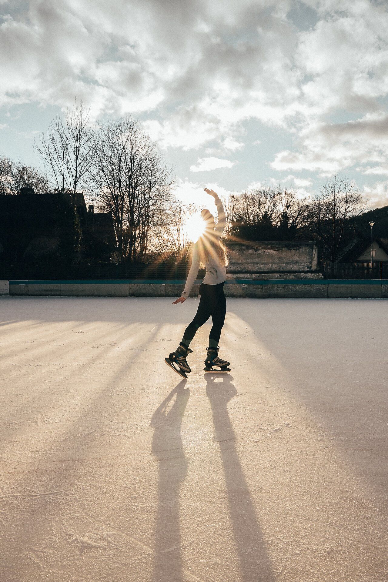 Ein strahlender Wintertag lädt zum Eislaufen ein, während die Sonne hinter den Bäumen aufgeht und eine magische Atmosphäre schafft. Die glitzernde Eisfläche spiegelt die warmen Farben des Himmels wider und verspricht unvergessliche Momente auf den Schlittschuhen.