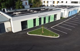 Außenansicht von modernen Ferienbungalows mit grünem und blauem Anstrich, Parkplatz und kleinem Rasenbereich.