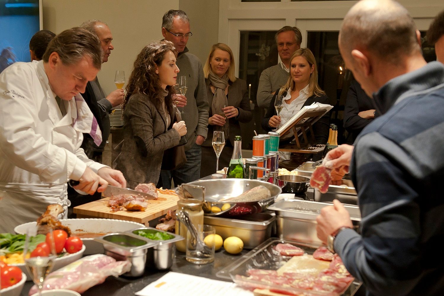 Ein Koch steht in einer Gastro-Küche, kocht und erklärt einer Gruppe