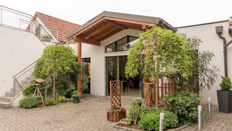 Eingang eines modernen Geb&auml;udes mit Pflanzen und &uuml;berdachtem Eingang.