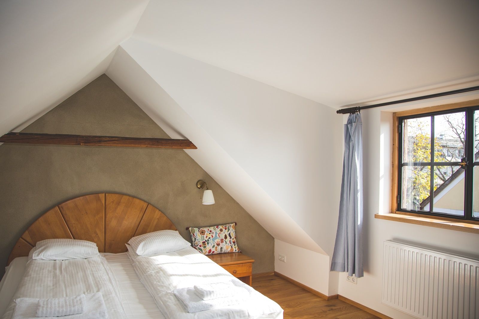 Gemütliches Schlafzimmer mit Dachschräge, Doppelbett, Holzdetails und Fenster mit Vorhang.
