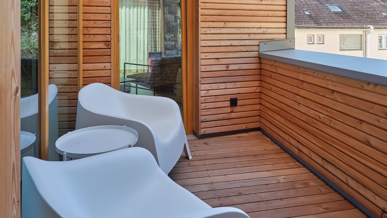 Moderner Balkon mit Holzw&auml;nden und wei&szlig;en St&uuml;hlen.