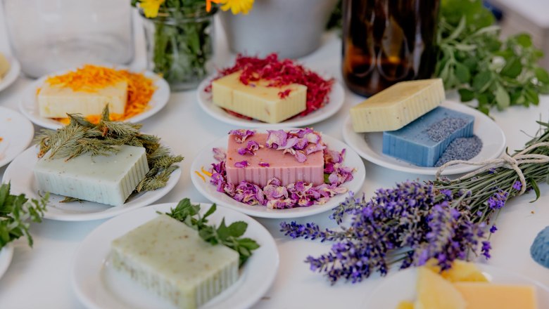 Verschiedene handgemachte Seifen auf Tellern, dekoriert mit Blumen und Kr&auml;utern.