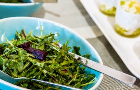 Schüssel mit Rucola-Salat und Besteck auf einem Tisch.