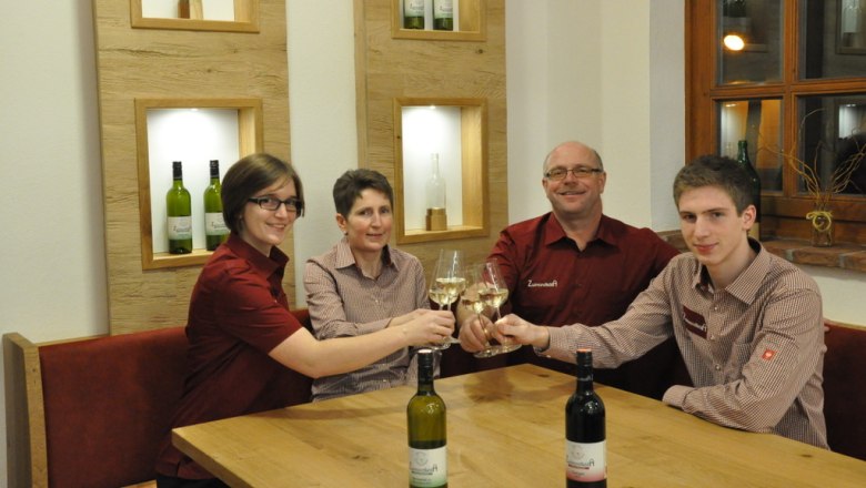 Vier Personen sto&szlig;en mit Weingl&auml;sern an einem Tisch an.