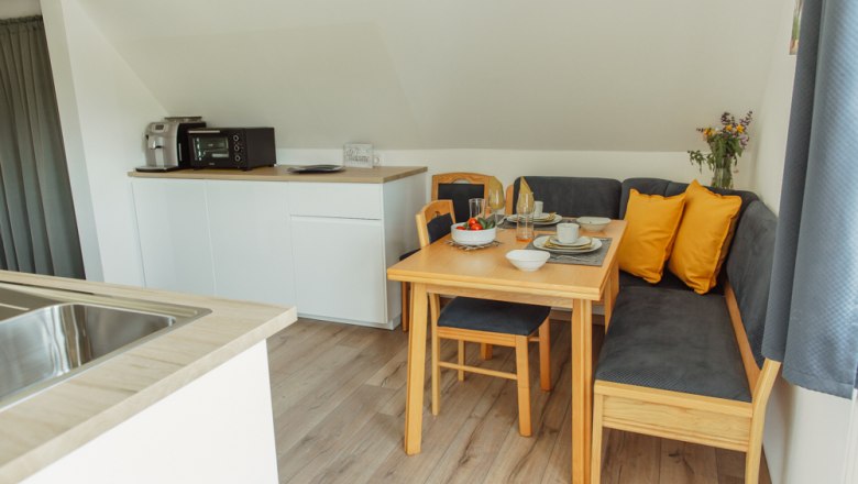 Gemütliche Essecke in einem modernen Appartement mit Holztisch, Eckbank und gelben Kissen.