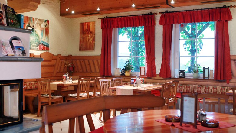 Gem&uuml;tlicher Innenraum eines traditionellen &ouml;sterreichischen Heurigen mit Holzm&ouml;beln und roten Vorh&auml;ngen.