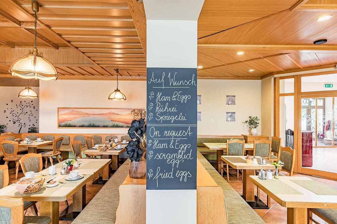 Frühstücksraum mit Holzmöbeln und einer Tafel mit Frühstücksoptionen.