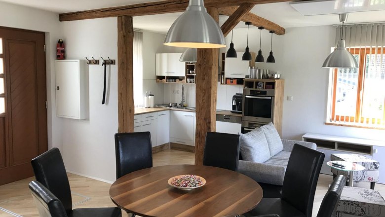 Moderner Wohnbereich mit Esstisch, Stühlen, Küche und Sofa.