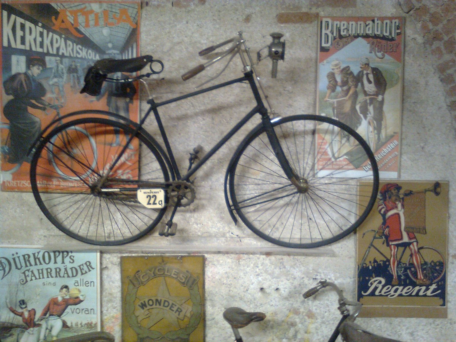 Altes Fahrrad an einer Wand mit Vintage-Werbeplakaten im Fahrradmuseum Schloss Vösendorf.