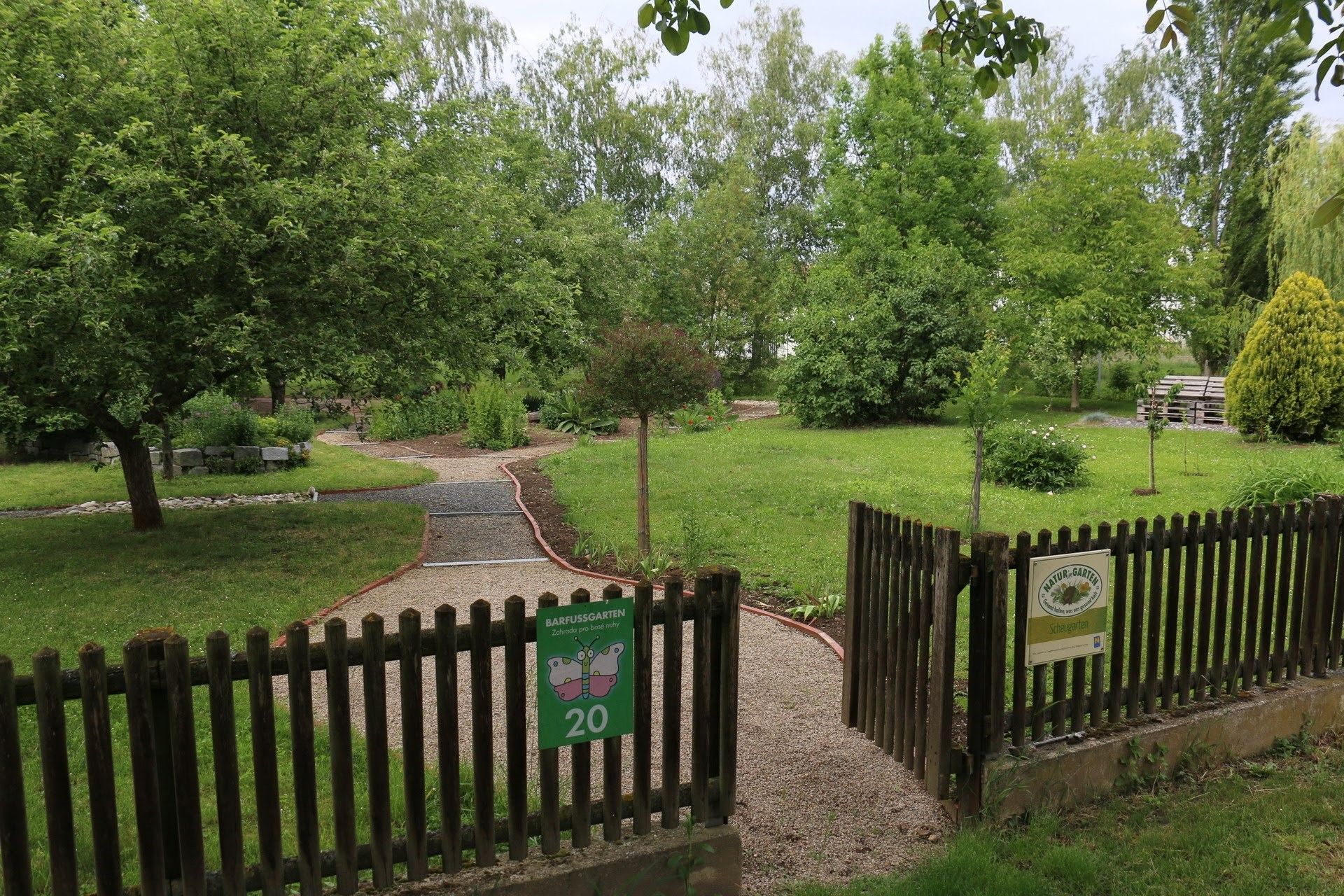 Eingang zu einem Barfußgarten mit Kiesweg und grüner Umgebung.