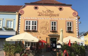 Fassade eines traditionellen Brauhauses mit Sonnenschirmen und Sitzbereich im Freien.