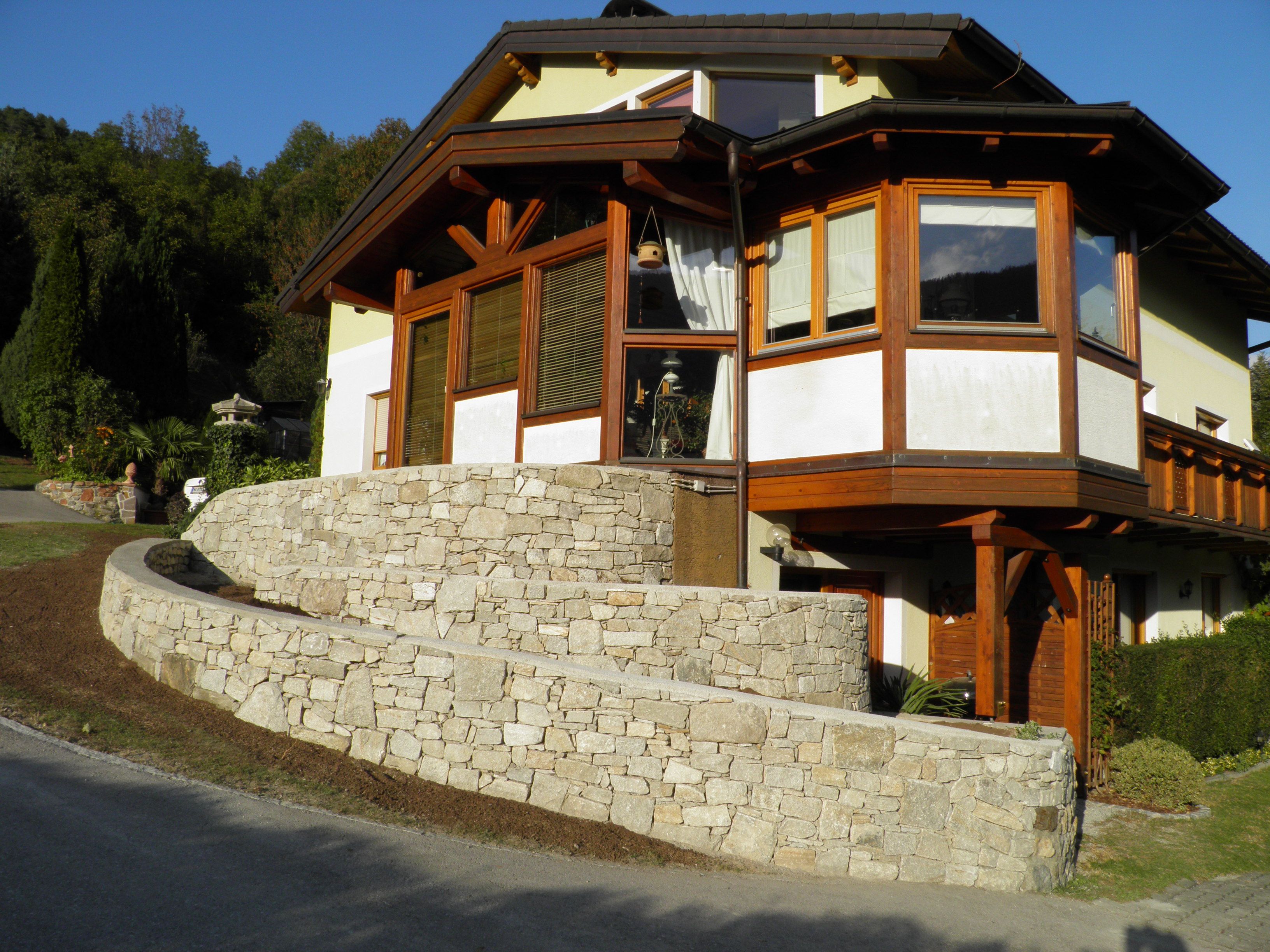 Haus mit Steinmauer und Holzverkleidung, umgeben von Bäumen.