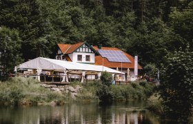 Gasthaus mit Solarpanelen und Zelt am Waldrand, nahe einem Teich.