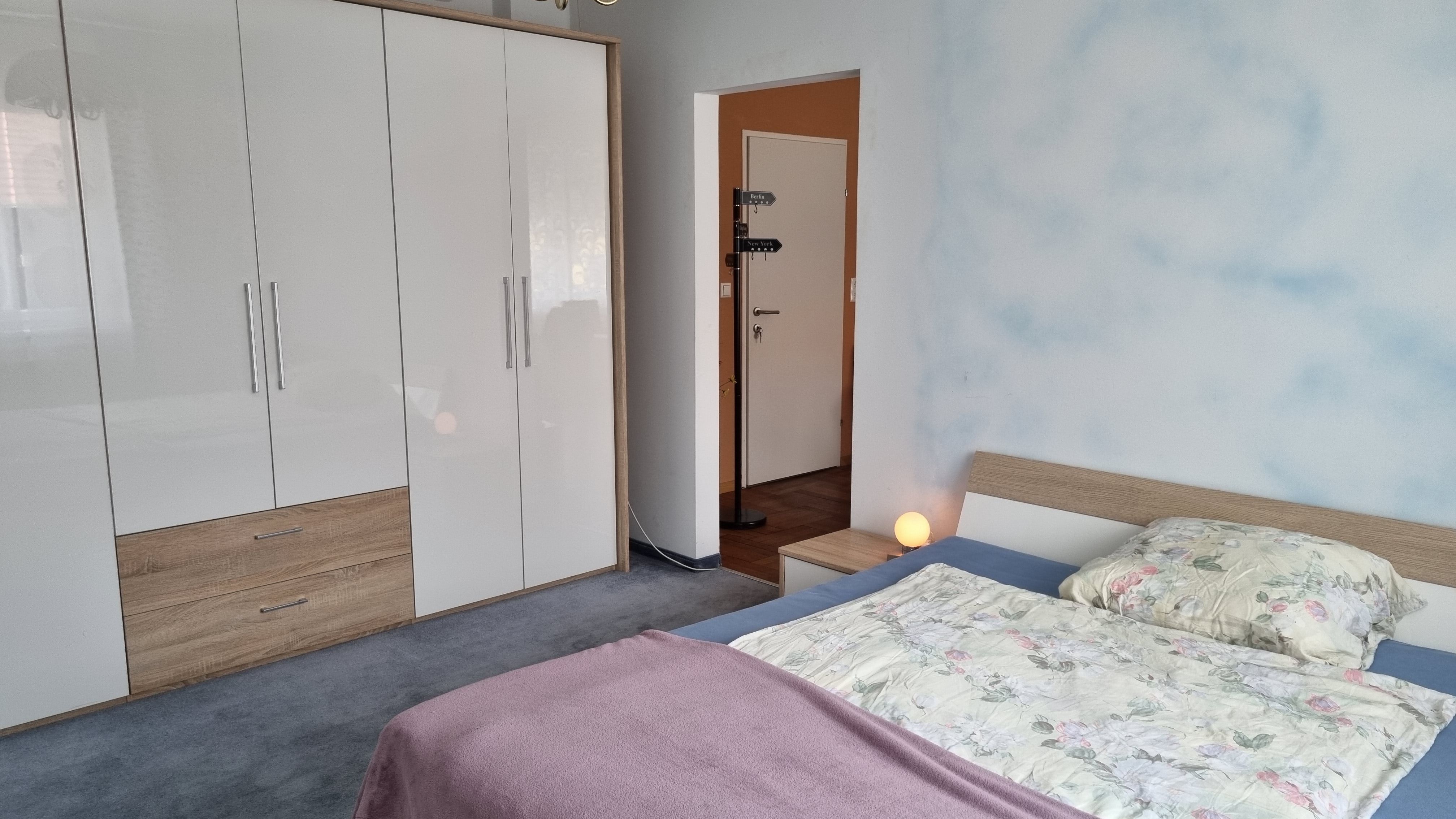 Ein Schlafzimmer mit einem Doppelbett, einem großen weißen Kleiderschrank und einer Nachttischlampe.