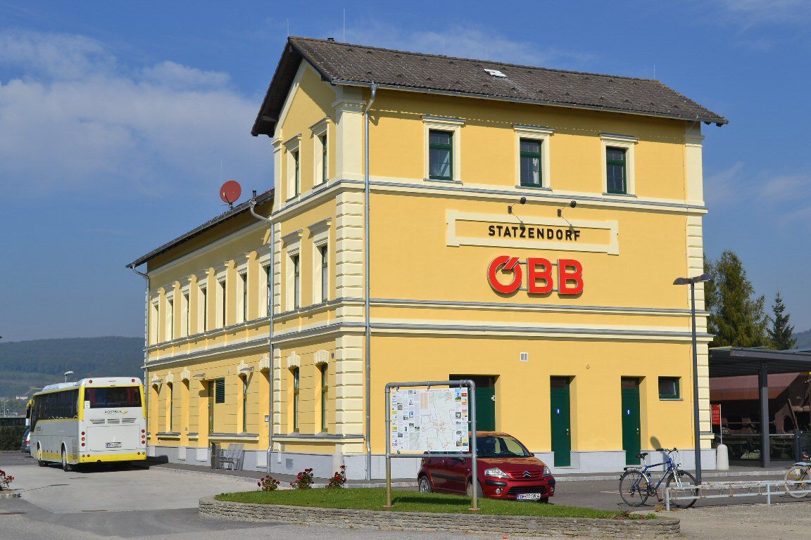 Gelbes Bahnhofsgebäude mit ÖBB-Logo und Bus im Vordergrund.