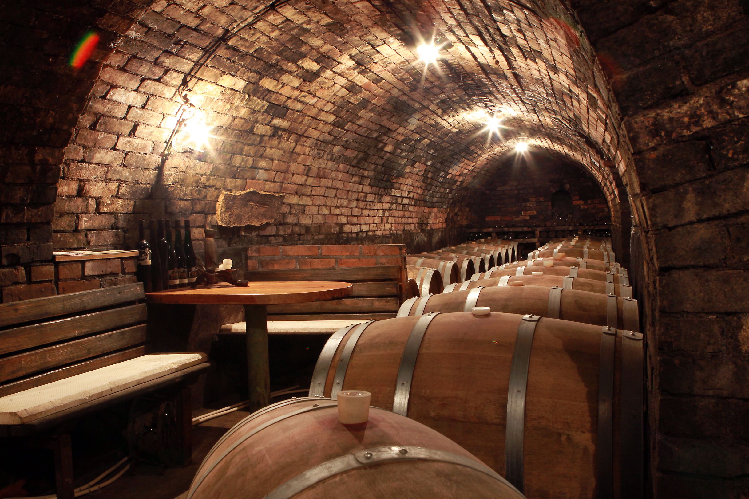 Ein Weinkeller mit Holzfässern und einem Tisch mit Bänken.