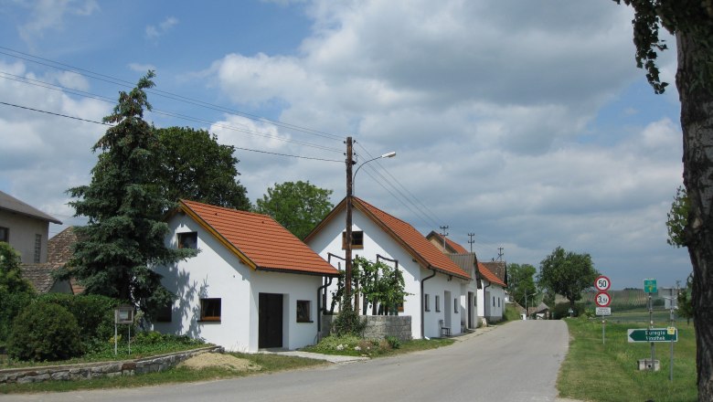 Kellergasse in Gro&szlig;kadolz mit wei&szlig;en H&auml;usern und rotem Dach entlang einer Stra&szlig;e.