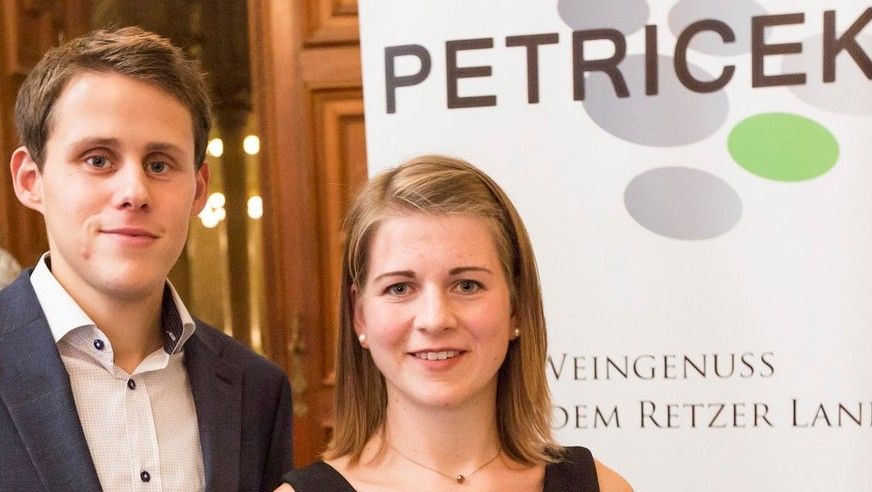 Zwei Personen vor einem Banner mit der Aufschrift 'PETRICEK'.