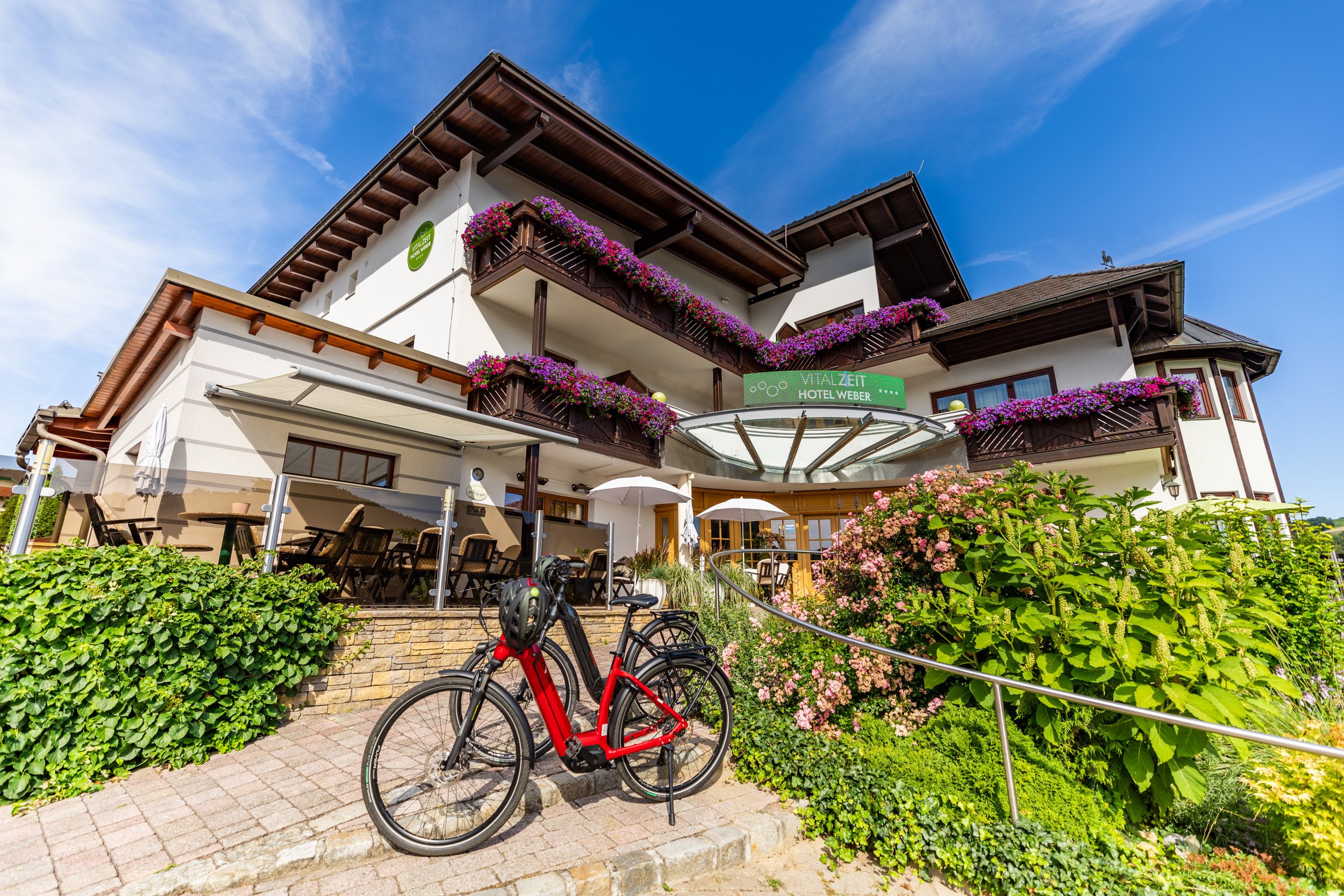 Außenansicht des Vitalzeit Hotel Weber mit Blumen und Fahrrad.