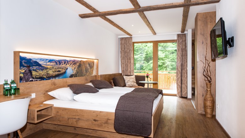 Modernes Hotelzimmer mit Holzmöbeln, großem Bett und Balkon mit Blick ins Grüne.