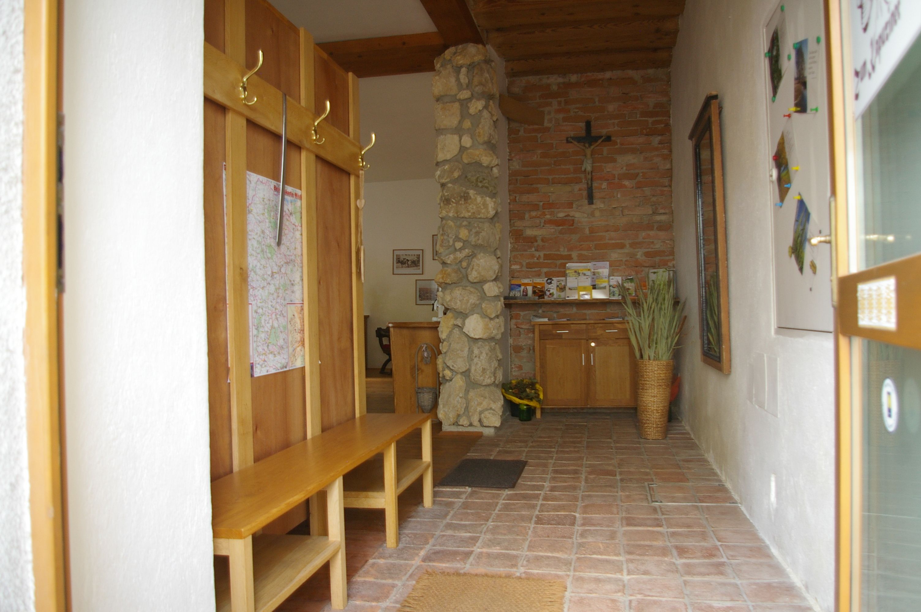 Eingangsbereich mit Holzbänken, Steinwand und Kreuz.