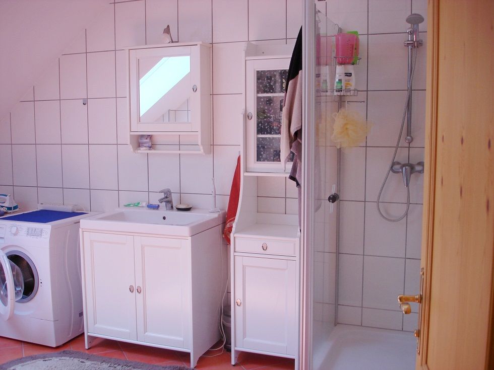 Badezimmer mit Waschmaschine, Waschbecken, Spiegel und Dusche.