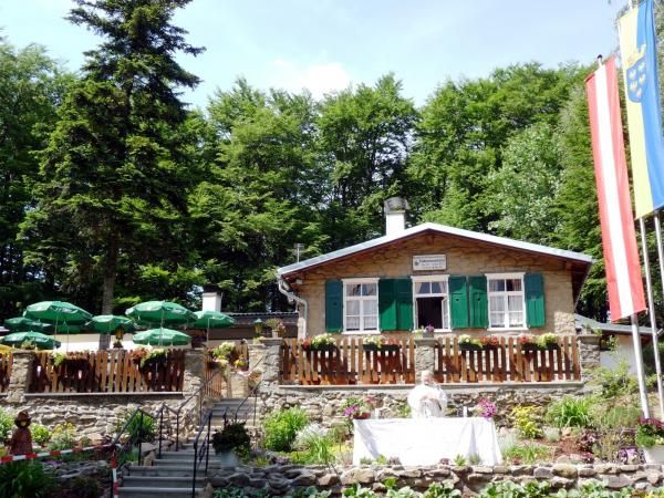 Eine Berghütte mit grünen Fensterläden, umgeben von Bäumen, mit einem Garten und Sonnenschirmen im Vordergrund.