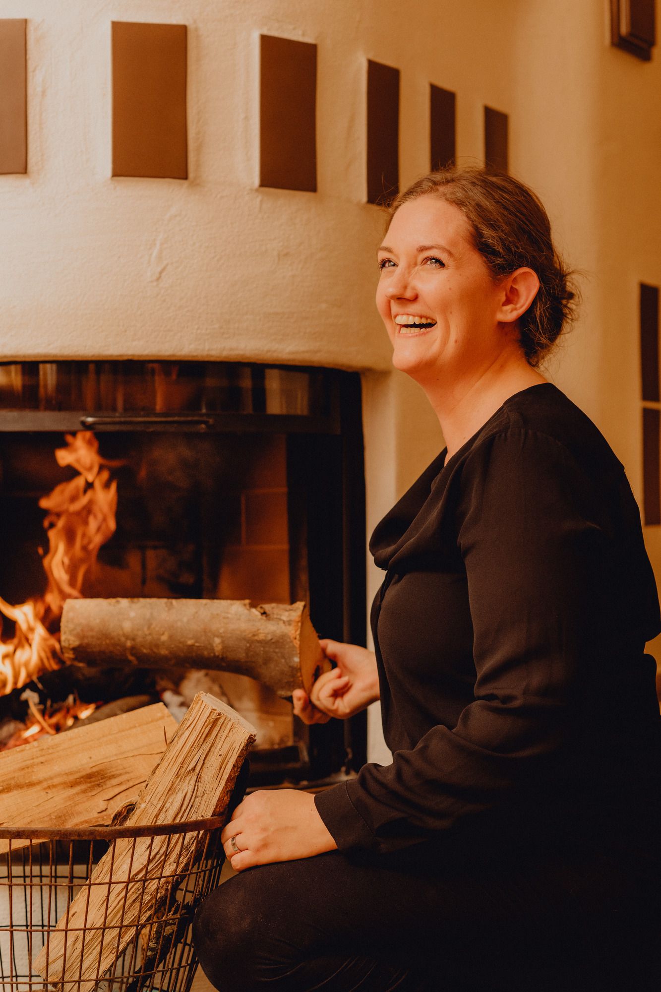 Frau lächelt vor einem Kamin mit brennendem Feuer.