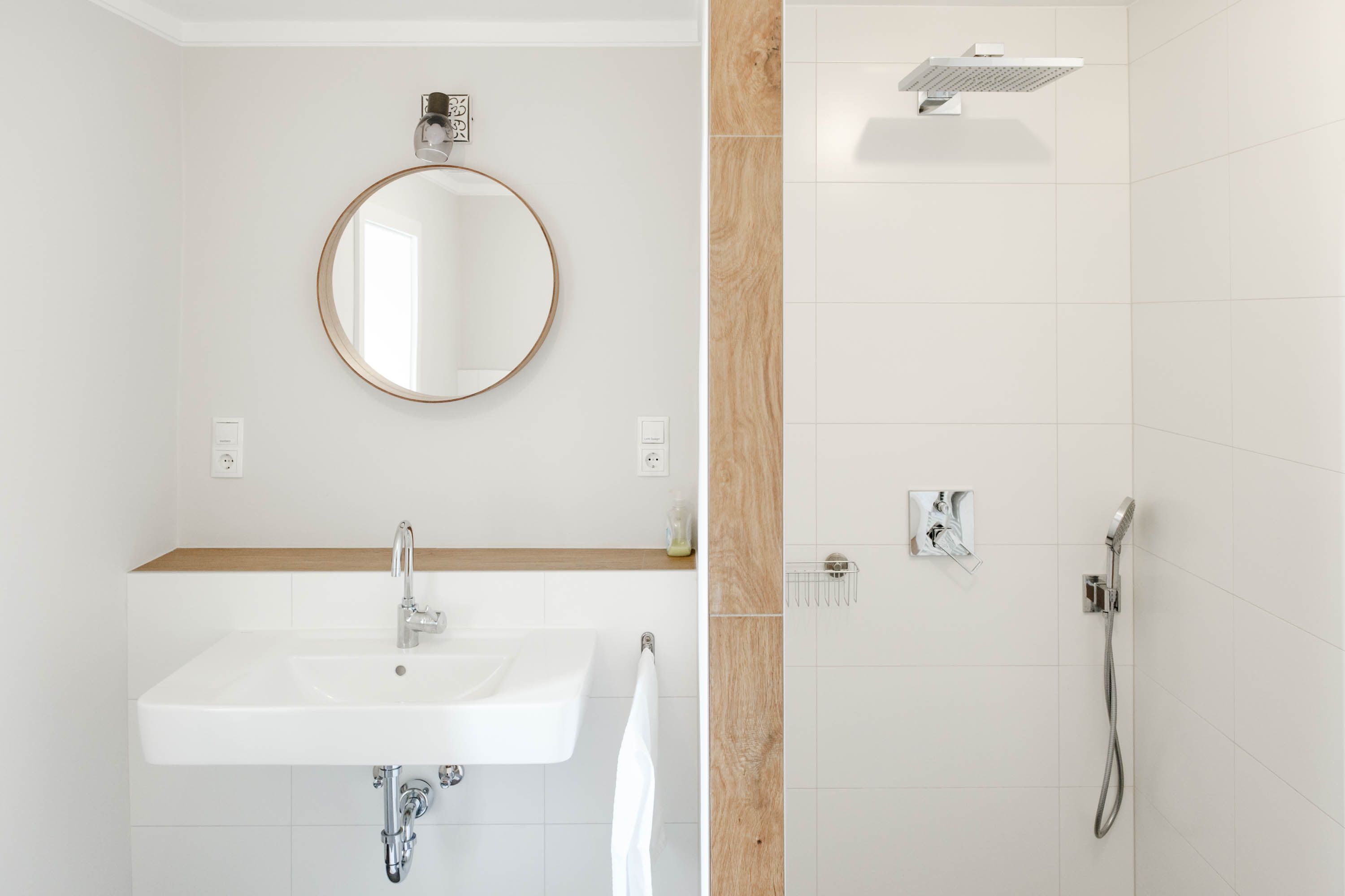 Modernes Badezimmer mit rundem Spiegel, Waschbecken und Dusche.