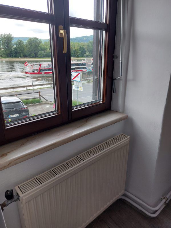 Blick aus einem Fenster auf einen Fluss mit einem vorbeifahrenden Boot und einem geparkten Auto.