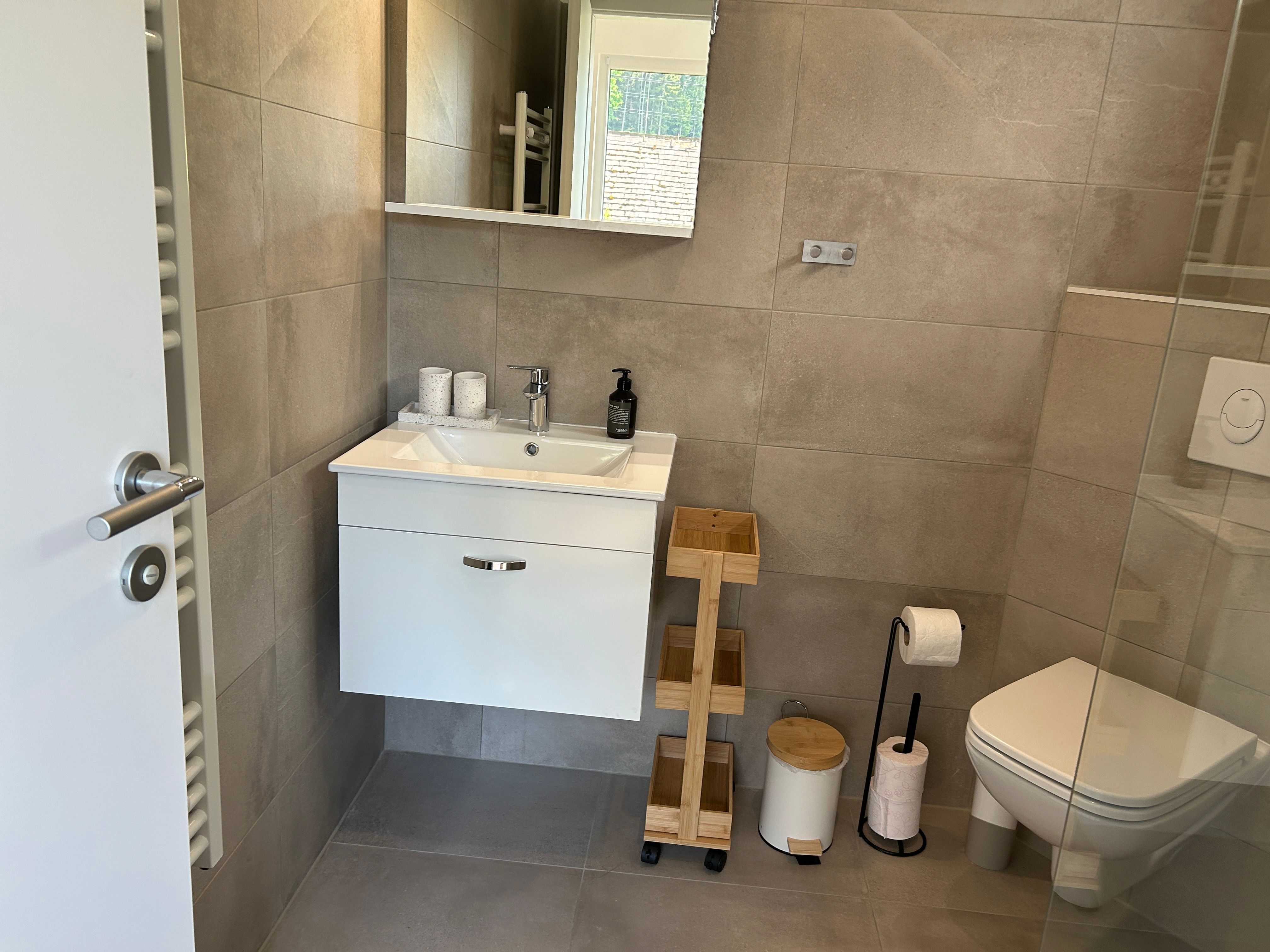 Modernes Badezimmer mit Waschbecken, Spiegel, Toilette und Regalen.