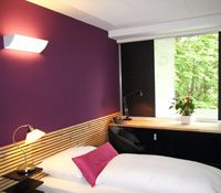 Modern eingerichtetes Zimmer mit lila Wand, Bett, Schreibtisch und Fenster mit Blick ins Grüne.