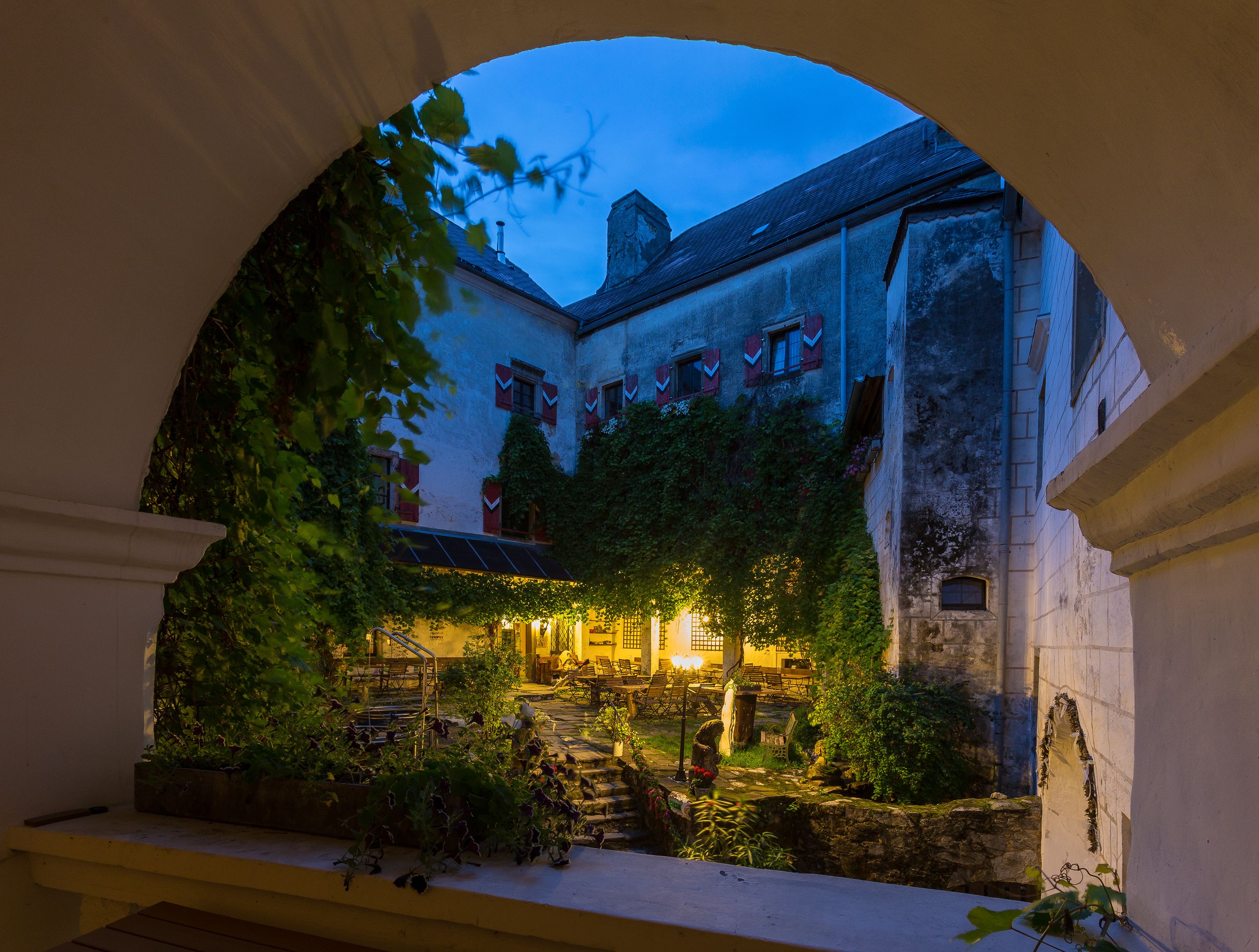 Innenhof der Burg Plankenstein bei Dämmerung, beleuchtet mit warmem Licht, umgeben von Efeu und alten Mauern.