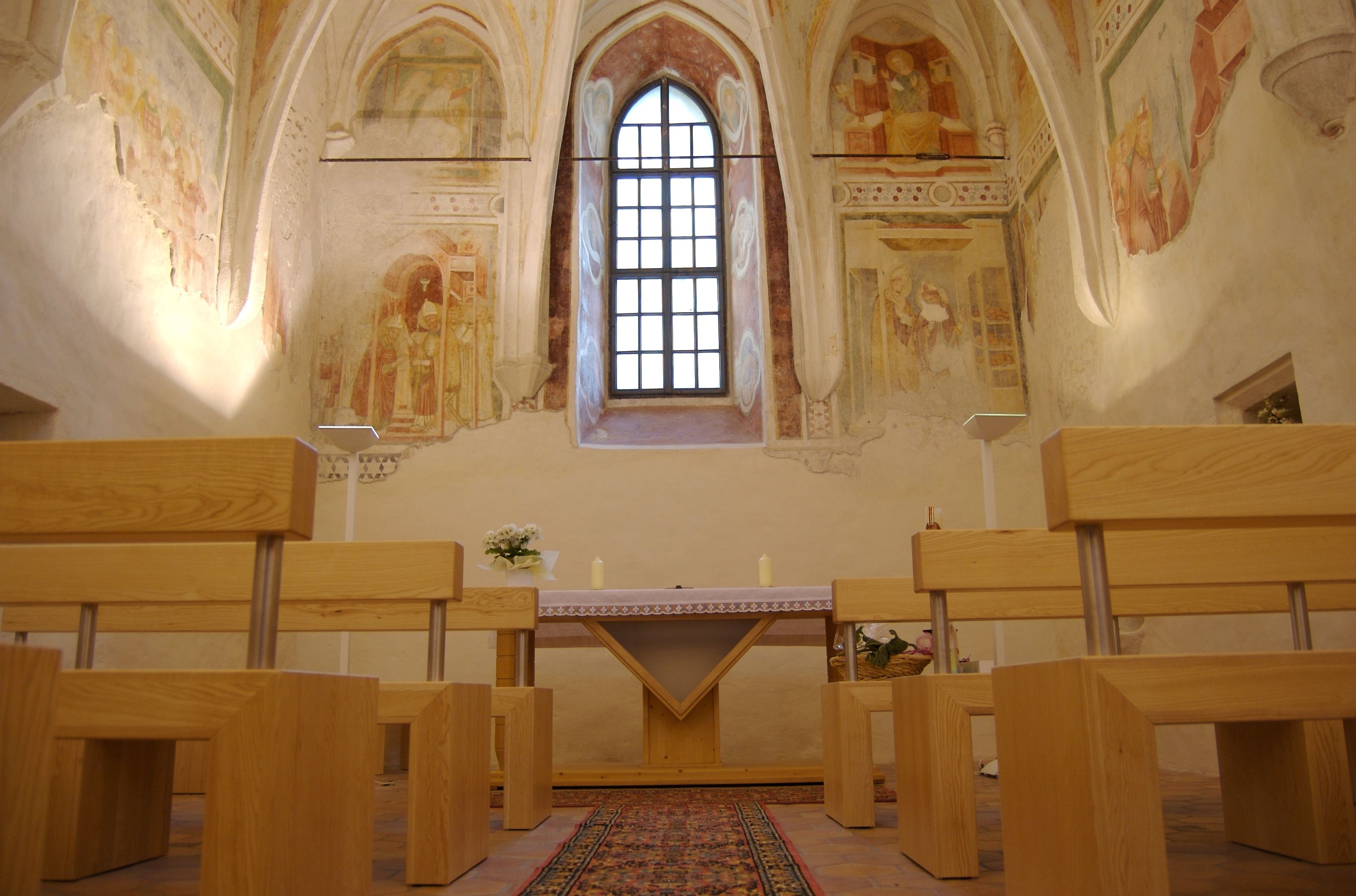 Innenansicht einer Schlosskapelle mit Fresken, Holzbänken und einem Altar.
