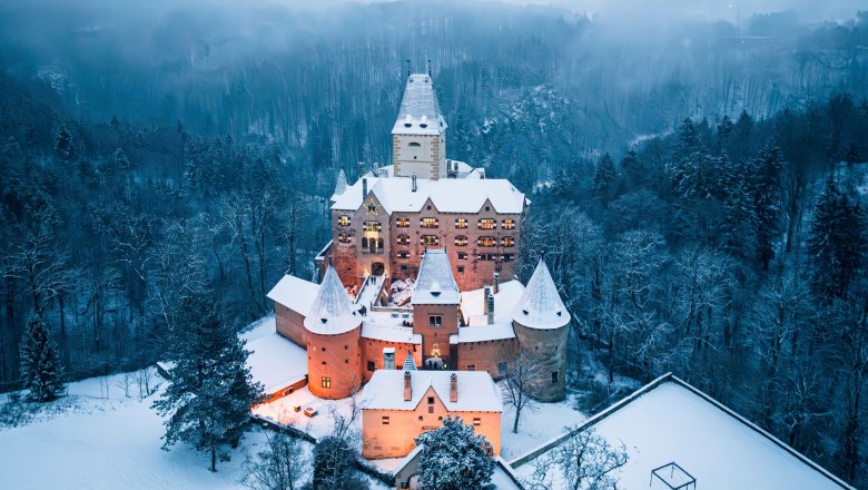 Luftaufnahme von Schloss Ottenstein im Winter, umgeben von schneebedeckten B&auml;umen und beleuchtetem Innenhof.
