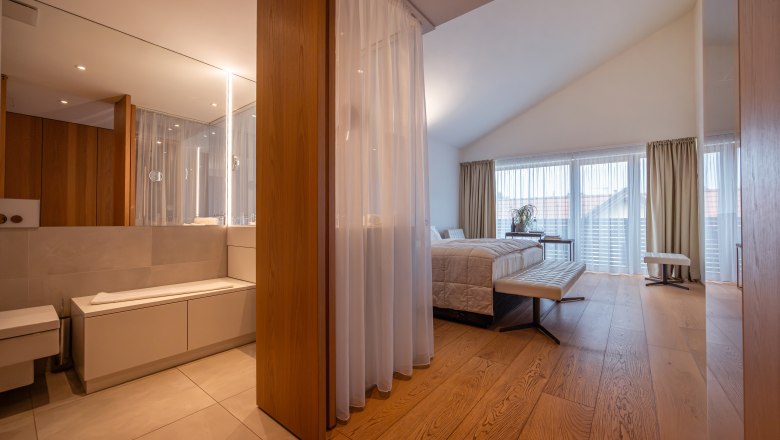 Modernes Hotelzimmer mit Holzfußboden, großem Bett und Badezimmer mit Spiegel.