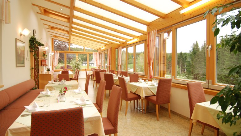 Ein heller Wintergarten eines Restaurants mit gedeckten Tischen und Blick auf einen Wald.