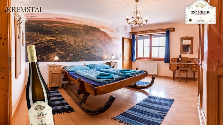 Gemütliches Zimmer mit Schlittenbett, Holzmöbeln und großem Wandbild. Eine Weinflasche steht im Vordergrund.