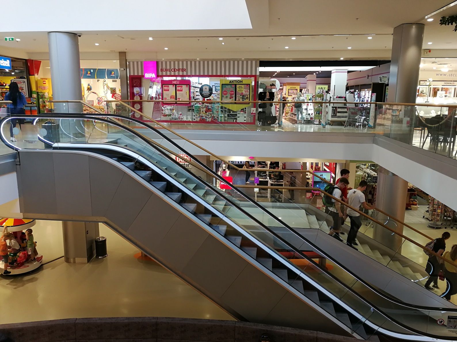 Innenansicht eines Einkaufszentrums mit Rolltreppen und Geschäften.