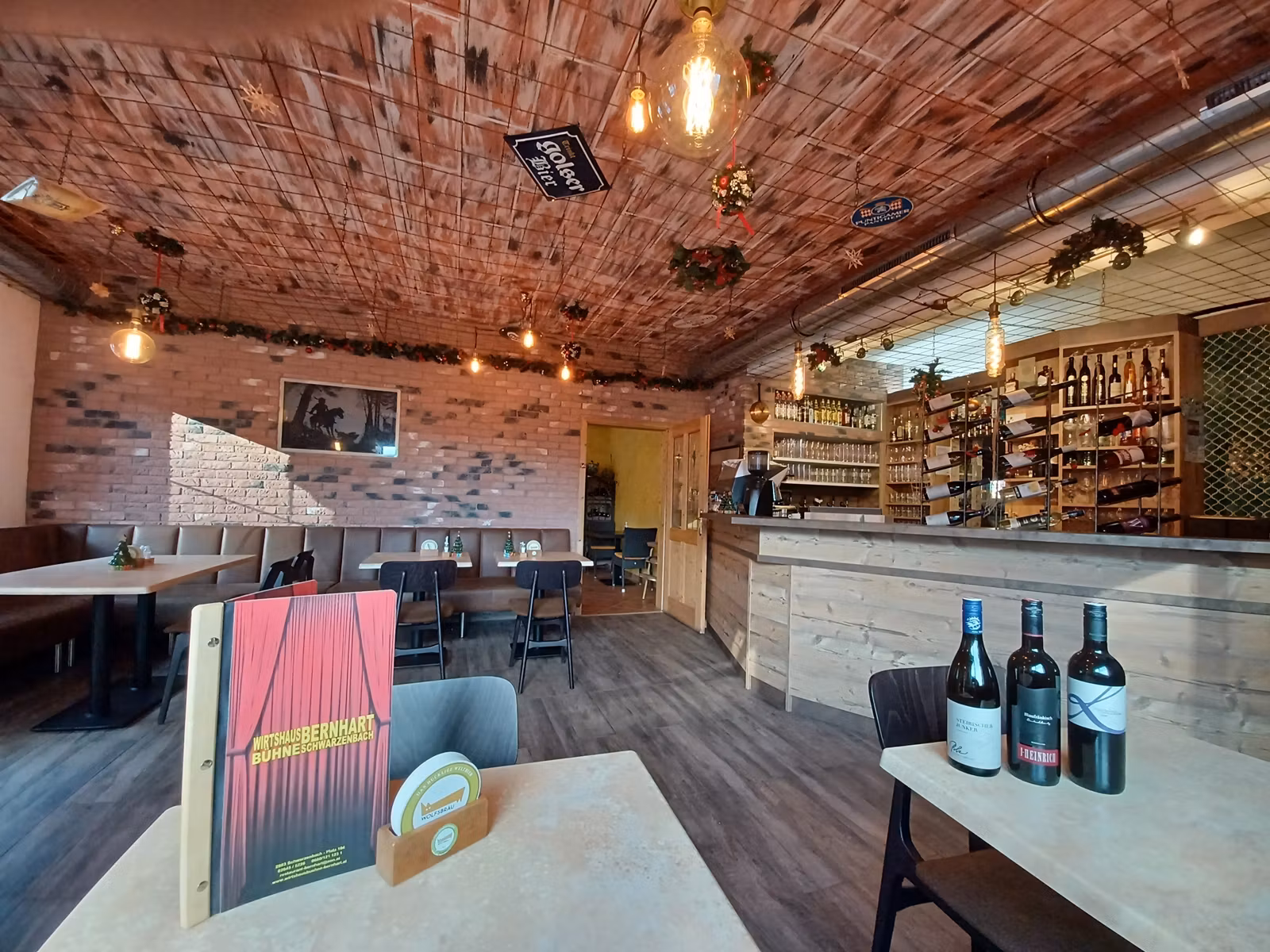 Gemütliche Gaststube mit Holztischen, Bar und Weinflaschen.